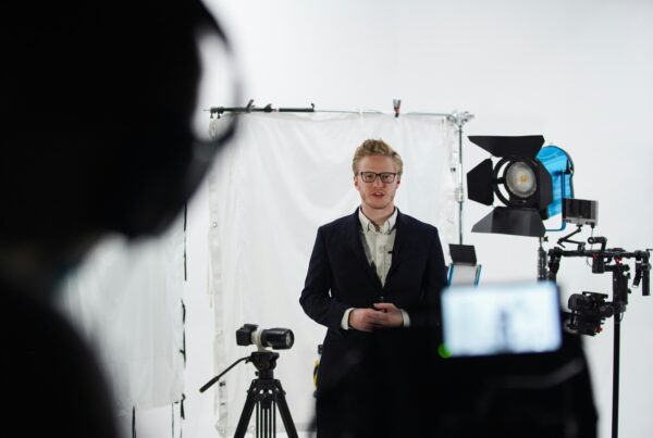 Man wearing a suit filming a video with the help of a teleprompter and recording devices in a studio