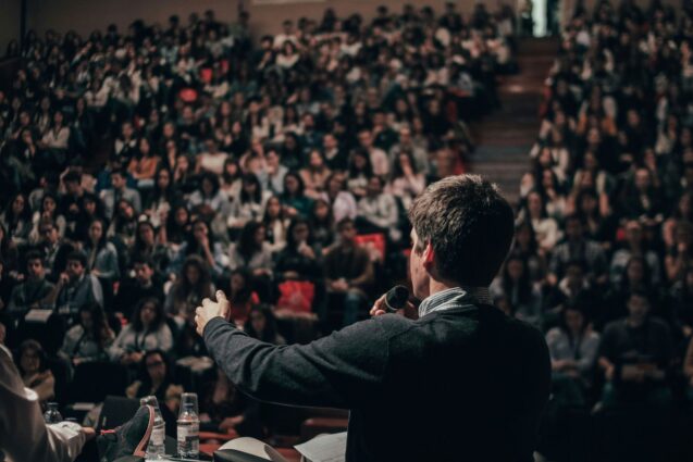 Man delivering a speech in front of a room full of people