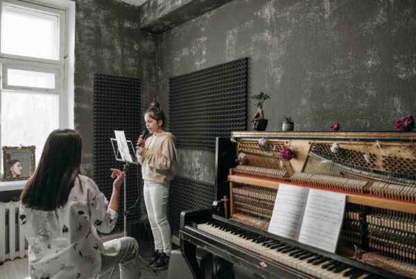 A vocal coach teaching a young girl on singing with a grand piano on the room