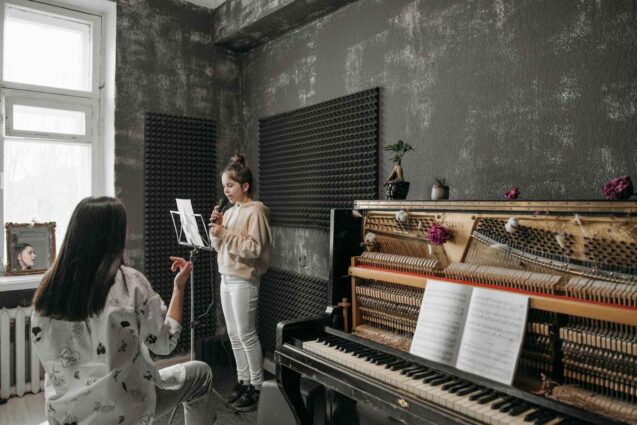 A vocal coach teaching a young girl on singing with a grand piano on the room