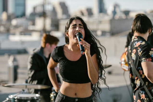 A woman passionately sings into a microphone while standing on a rooftop