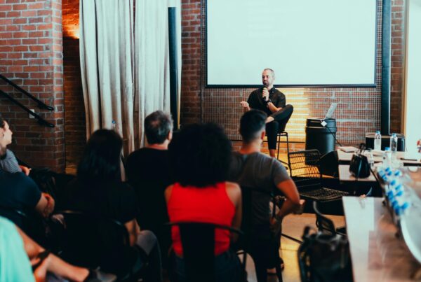 A man sitting while speaking in front of his audience