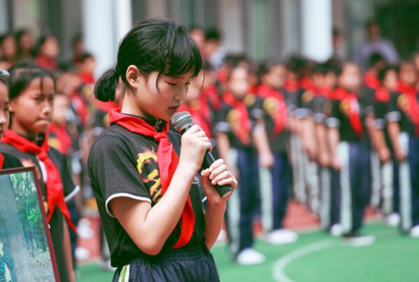 Young girl wearing sports clothes, holding a mic during a school assembly