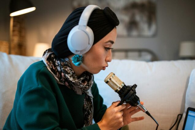 A woman in a turban and headphones sits comfortably on a couch, enjoying her music or podcast