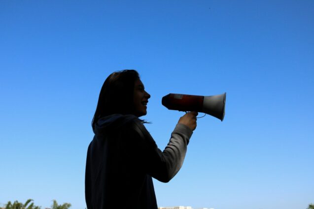 A woman’s silhouette energetically shouting into a megaphone