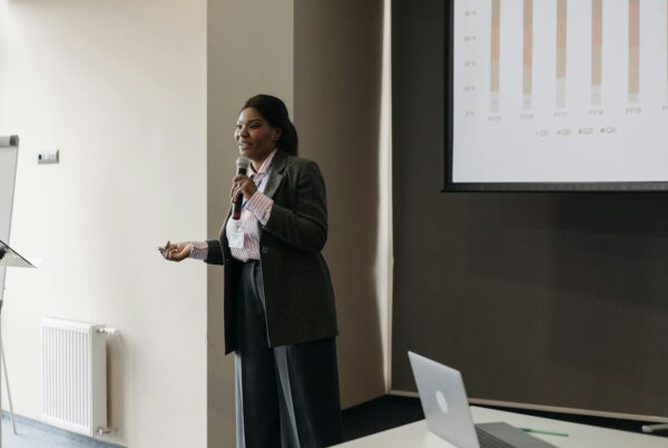 A woman presenting in front of a large screen, engaging her audience with visual aids and confident body language