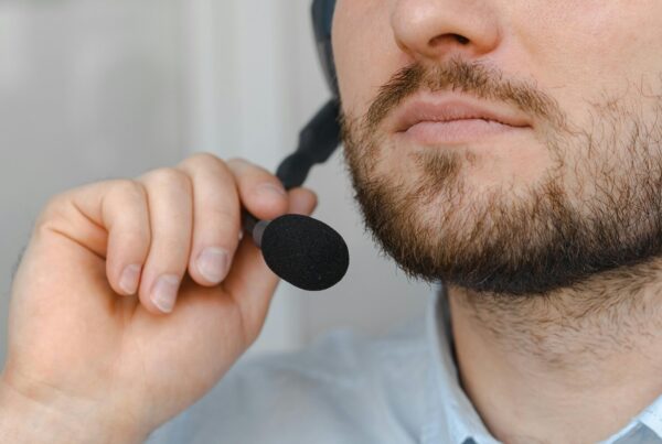 A close-up of a man adjusting a headset microphone while holding the mic with one hand