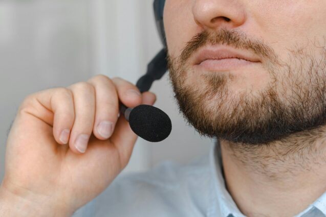 A close-up of a man adjusting a headset microphone while holding the mic with one hand