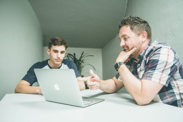 A man and a young man having a discussion in front of a laptop in a modern meeting space.