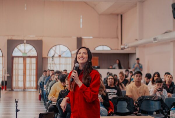 A woman in a red jacket is delivering a speech into a microphone