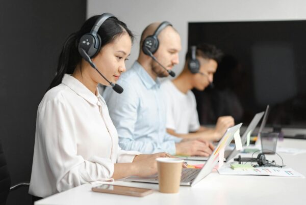 A group of people with headsets working together in an office, typing on laptops