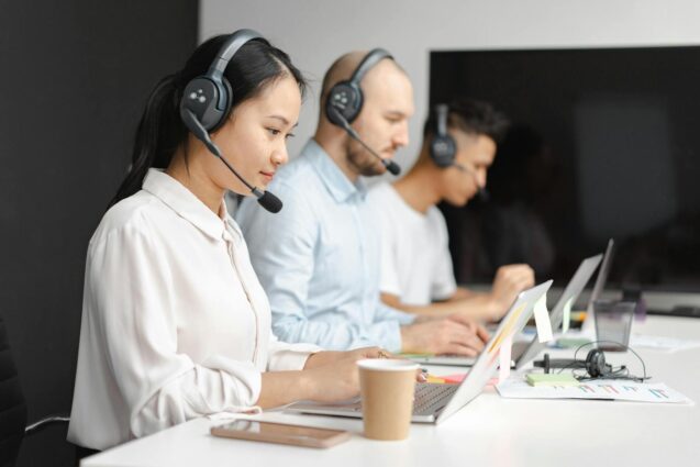 A group of people with headsets working together in an office, typing on laptops