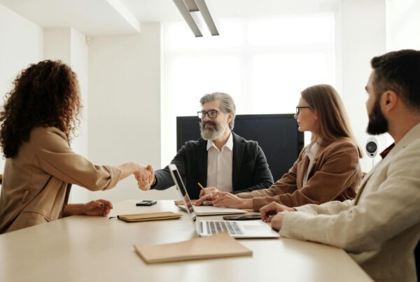 A woman shaking hands with a man in a business meeting with other colleagues observing